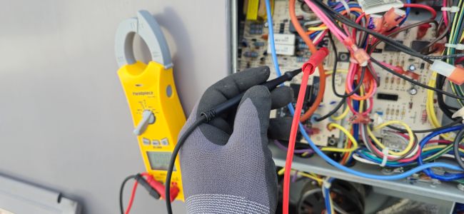 Commercial HVAC technician testing electrical components inside a rooftop unit control panel. Commercial HVAC Services