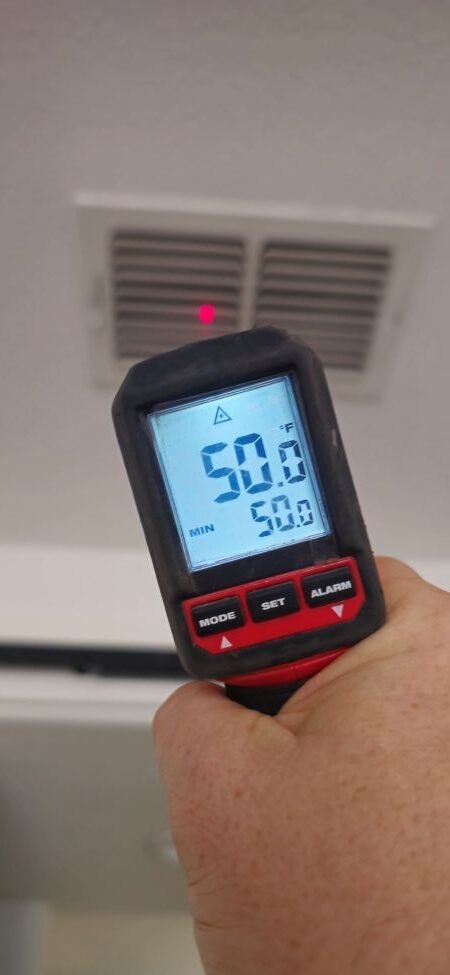Digital infrared thermometer displaying 50.0°F while measuring supply air from an HVAC ceiling vent.