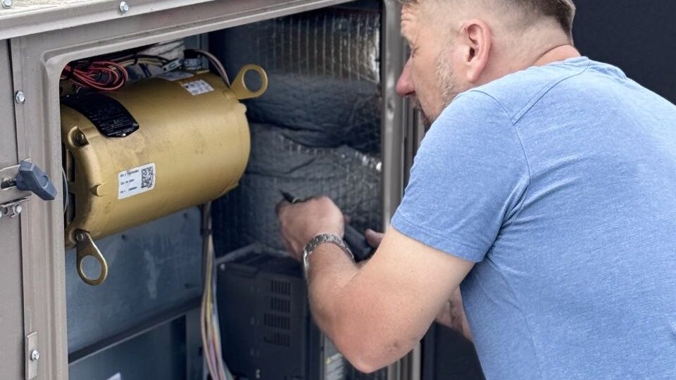 Levano Pro HVAC technician working inside an open HVAC cabinet with a screwdriver