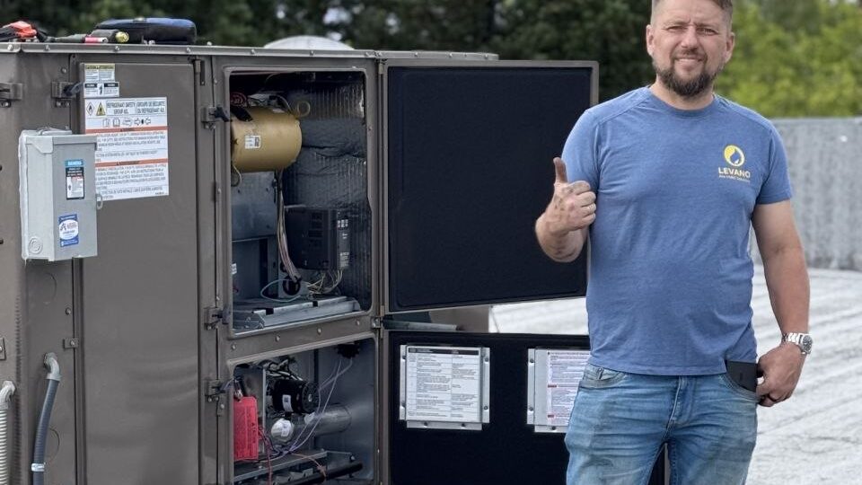 Levano Pro HVAC technician giving a thumbs up beside an open package unit showing its components