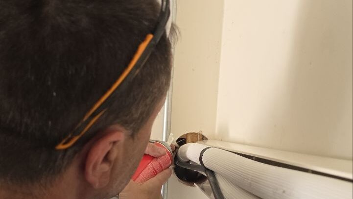 Levano Pro HVAC technician sealing around a ductless line set where it enters the house