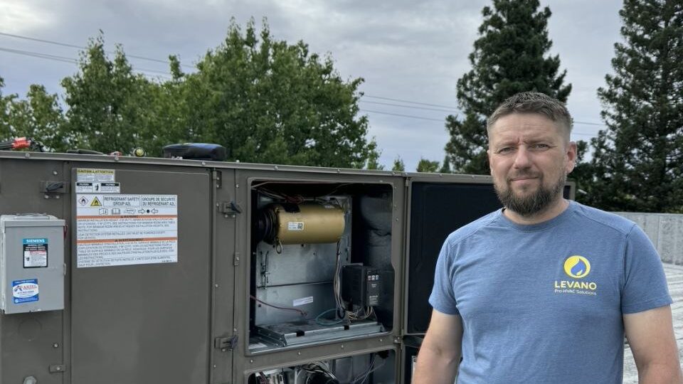 Levano Pro HVAC technician in front of a large rooftop central air unit with trees behind