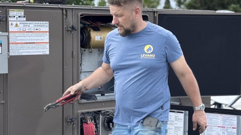 Levano Pro HVAC technician on a flat roof carrying tools to an open HVAC unit