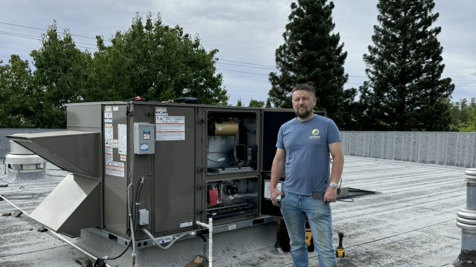 Levano Pro HVAC technician next to a rooftop heat pump unit with tall pines behind