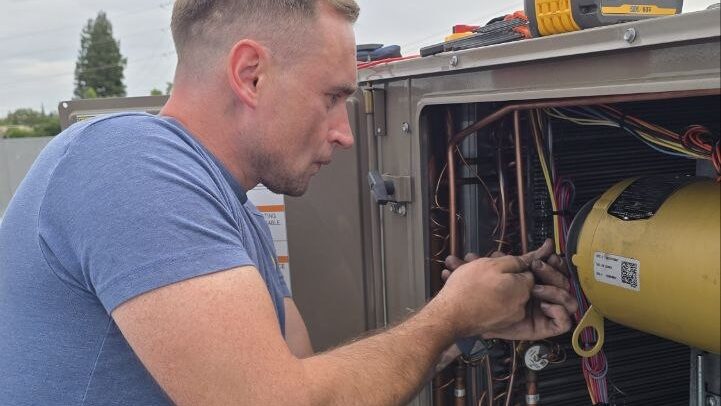 Levano Pro HVAC technician checking wiring and refrigerant lines inside an open heat pump unit