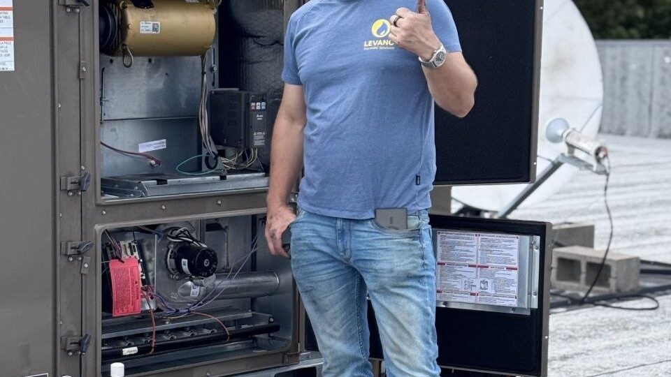 Levano Pro HVAC technician standing beside an open heat pump unit on a roof
