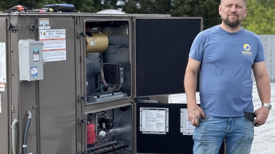 Levano Pro HVAC technician standing beside an open packaged HVAC unit on a commercial roof